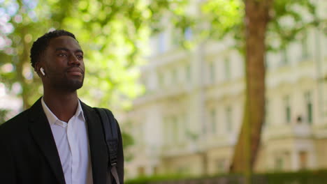 young businessman wearing wireless earbuds streaming music or podcast from mobile phone walking to work in offices in the financial district of the city of london uk 4