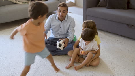 papá enseñando a los hijos hermanos a lanzar una pequeña pelota de fútbol