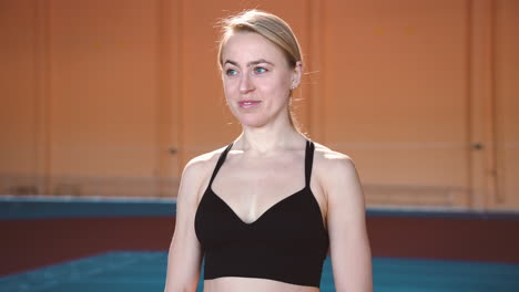 zoom in camera shot of a smiling blonde sportswoman standing in an indoor sport facility and looking at camera