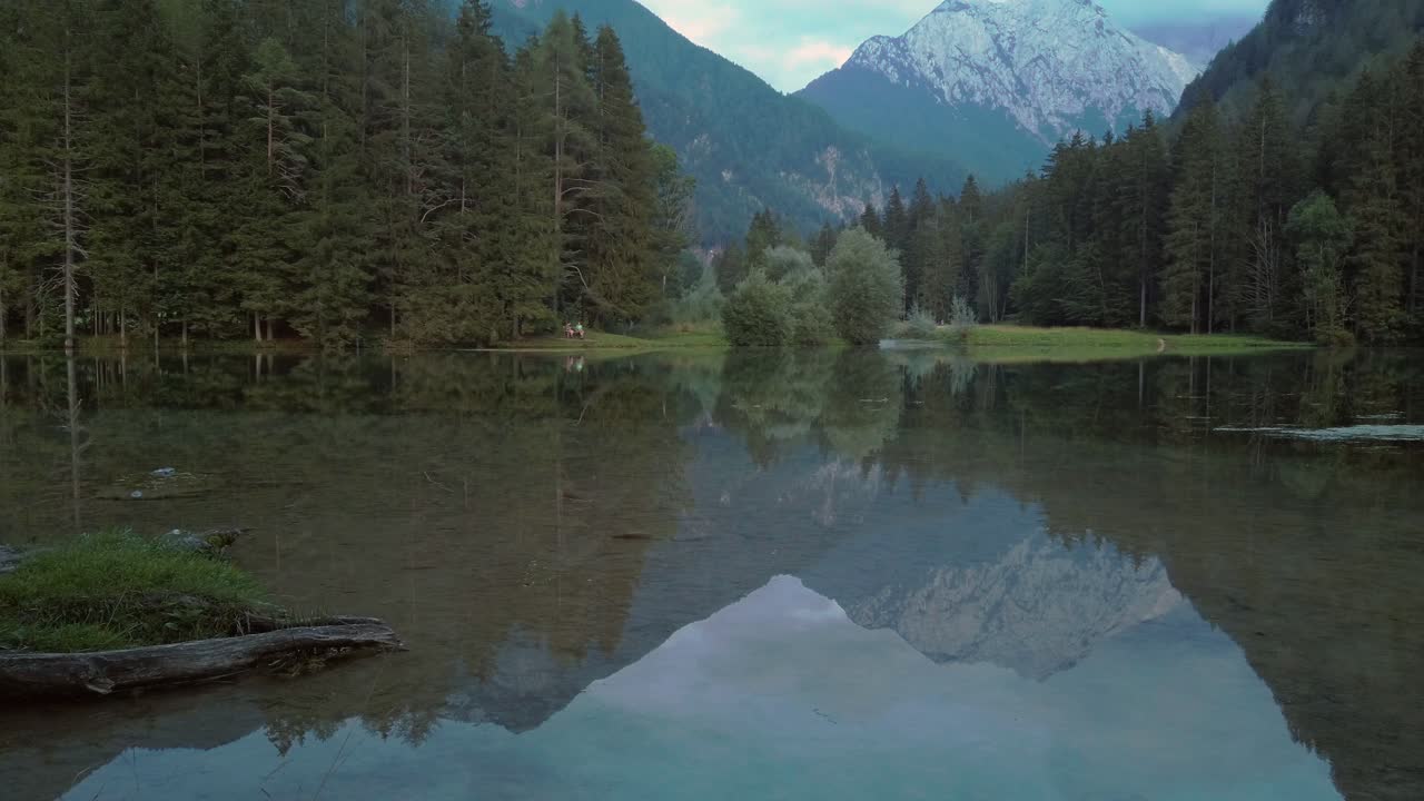 Alpine mountain range reflecting in lake Plansar or Plansarsko jezero in Jezersko, Slovenia in autumn, panning shot