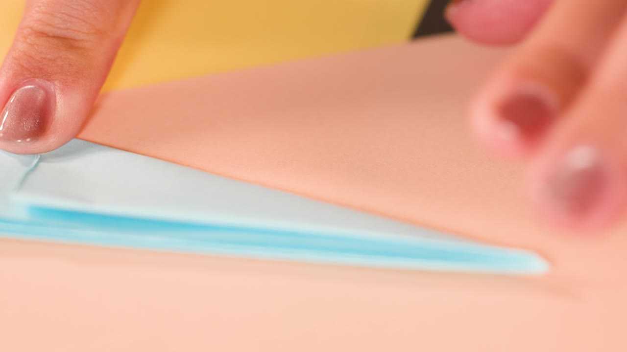 Close-up shot of fingers with metallic nail polish precisely folding blue paper for origami art