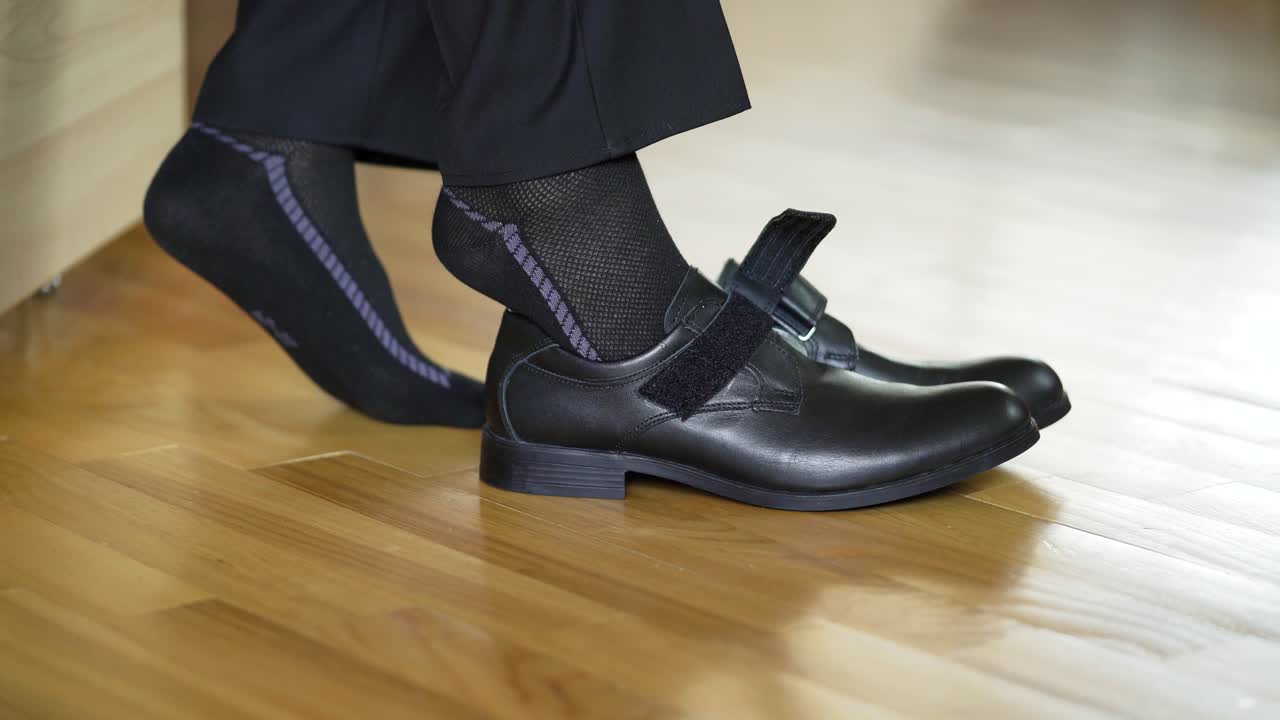 Teens legs are putting on new fashion shoes with the help of a shoe spoon on parquet. A boy in black socks puts on school shoes on the brown floor background indoors at home.
