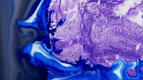 Video-of-close-up-of-metallic-purple,-blue-and-white-ink-in-water-with-copy-space