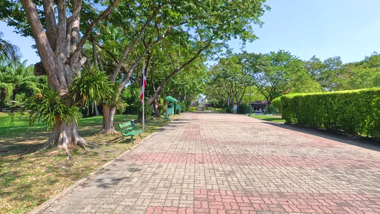 A tranquil brick path lined with lush greenery and benches under clear skies in Bangkok's Rama IX Park