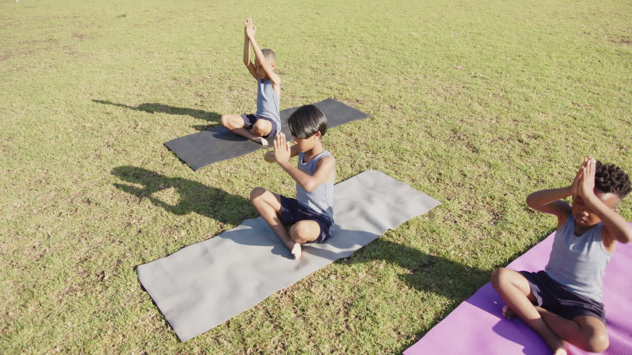 Practicing yoga on mats, children meditating outdoors during school activity
