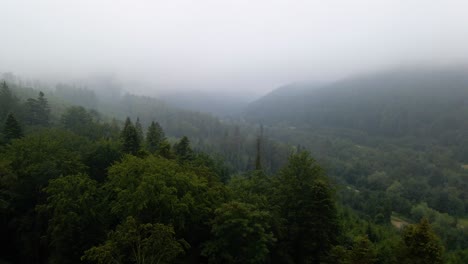 Vista-Aérea-Sobre-Montañas-Y-Bosques-Nublados,-Un-Pueblo-En-El-Fondo,-En-Las-Montañas-De-Los-Cárpatos,-Ucrania---Reversa,-Disparo-De-Drones