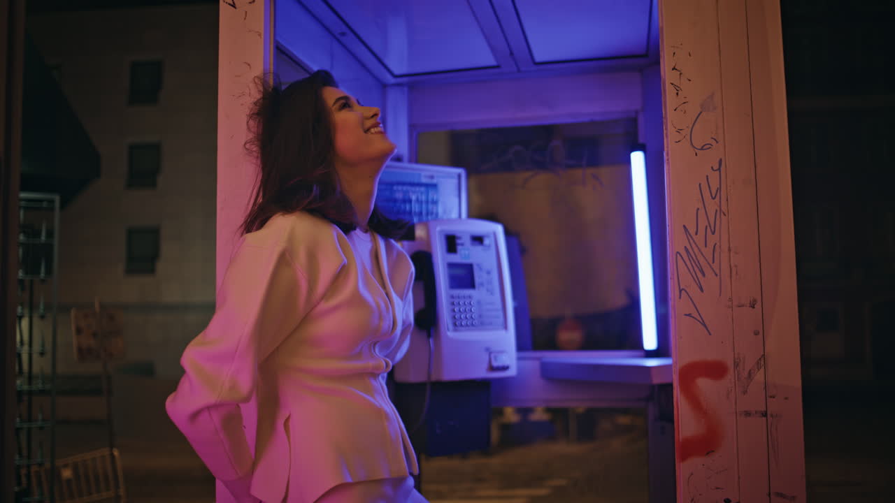 Laughing girl resting neon telephone cabin wall closeup. Model looking camera