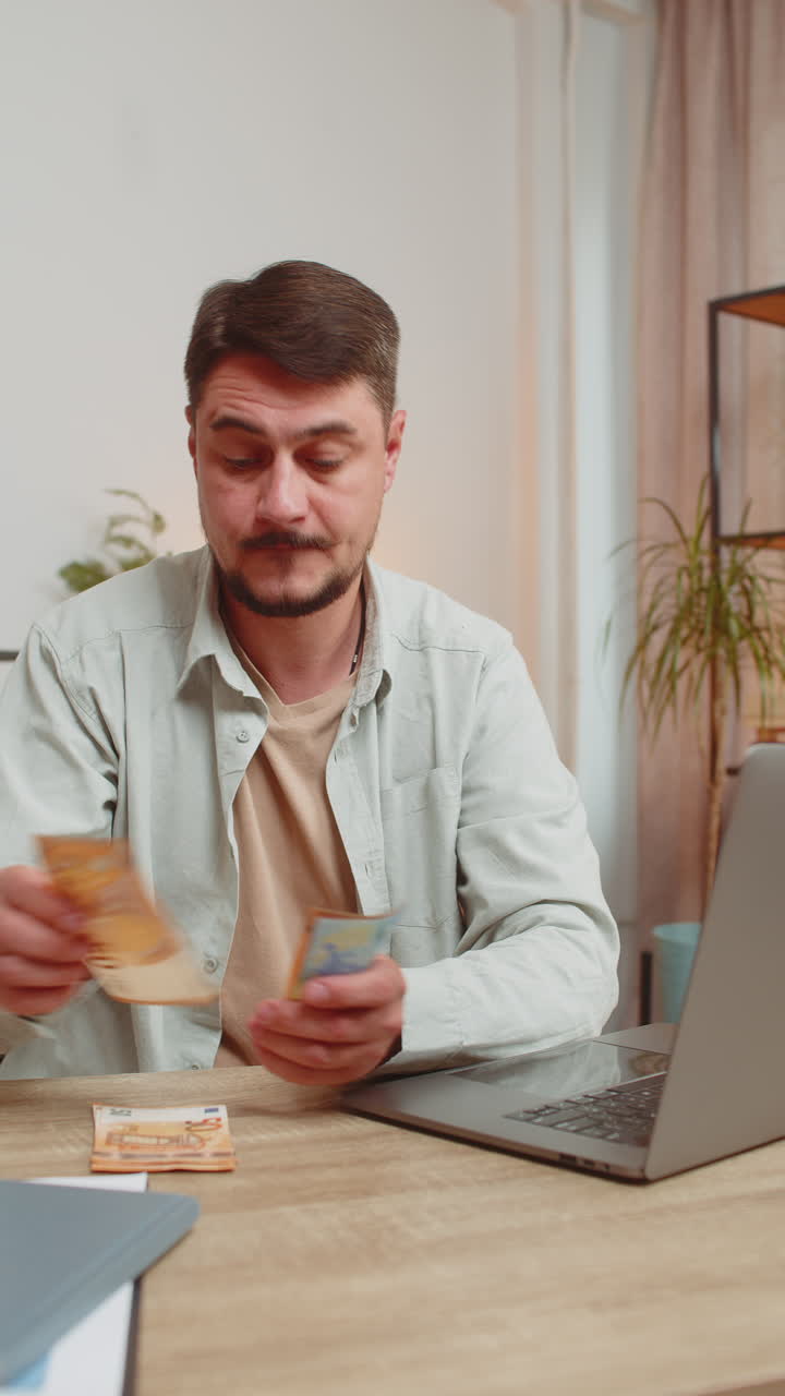 Rich happy caucasian man counting money cash using laptop calculate domestic bills at home table