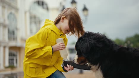 Happy-teenage-girl-feeds-her-dog-from-a-special-drinking-bowl-during-a-walk-after-the-rain