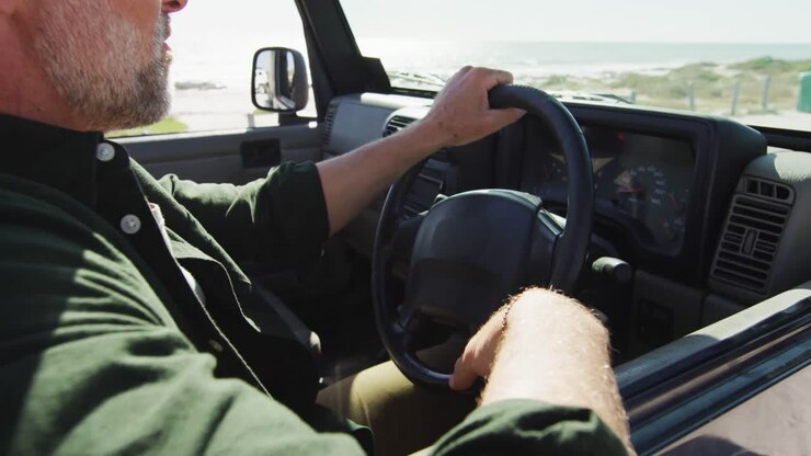 Uomo caucasico seduto in auto che ammira il panorama in una giornata di sole al mare.