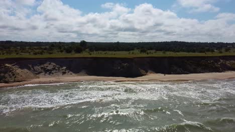 Flying-Over-Coastline-Baltic-Sea-Ulmale-Seashore-Bluffs-Near-Pavilosta-Latvia-and-Landslides-With-an-Overgrown,-Rippling-Cave-Dotted-Cliff-and-Pebbles