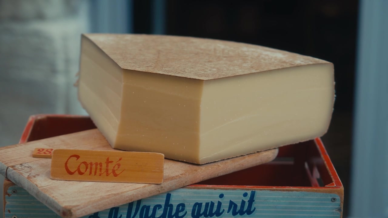 Primo piano di un grande spicchio di tradizionale formaggio francese Comté con un'etichetta di legno su una cassa d'epoca in un mercato nel sud della Francia