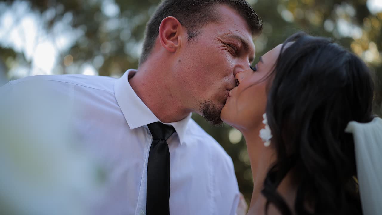 La telecamera si avvicina e si allontana da giovani sposi che si baciano a un matrimonio.