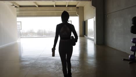 woman with a fitness mat walks through an empty gymnasium fitness center to start the exercise routine.