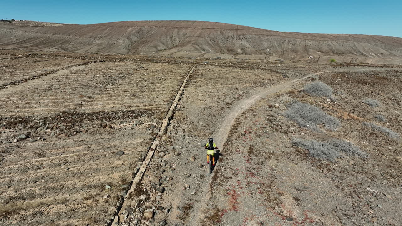 disparo aéreo de un hombre montando su bicicleta de montaña cuesta arriba en un paisaje desértico