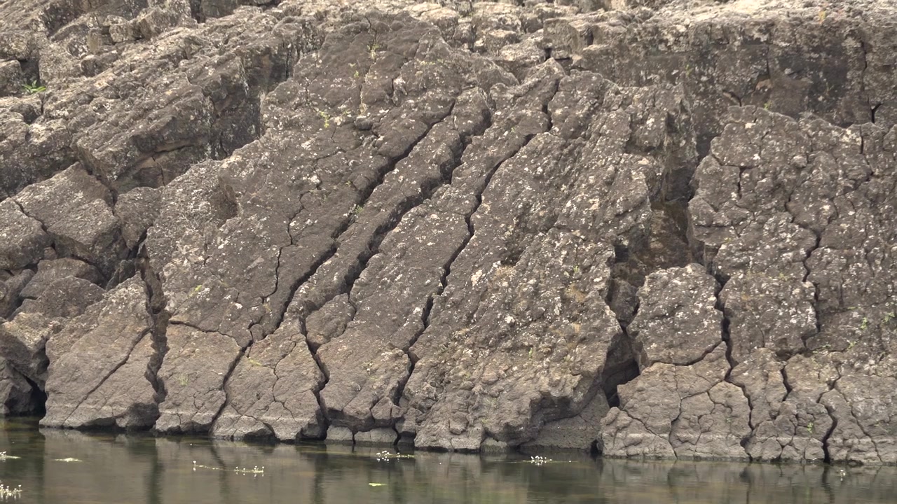 Formación rocosa volcánica agrietada a lo largo de la orilla de un río tranquilo