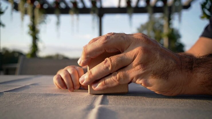 Reaching adult hand in dark shirt covering nudging wooden block on patio table while child watching