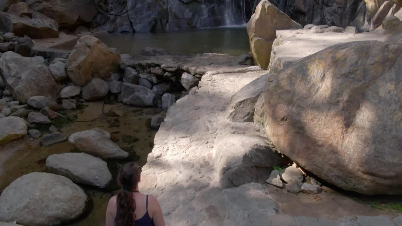 Woman Sitting On a Rock Admiring The Beauty Of Cascada de Yelapa In Jalisco, Mexico. - aerial tilt up