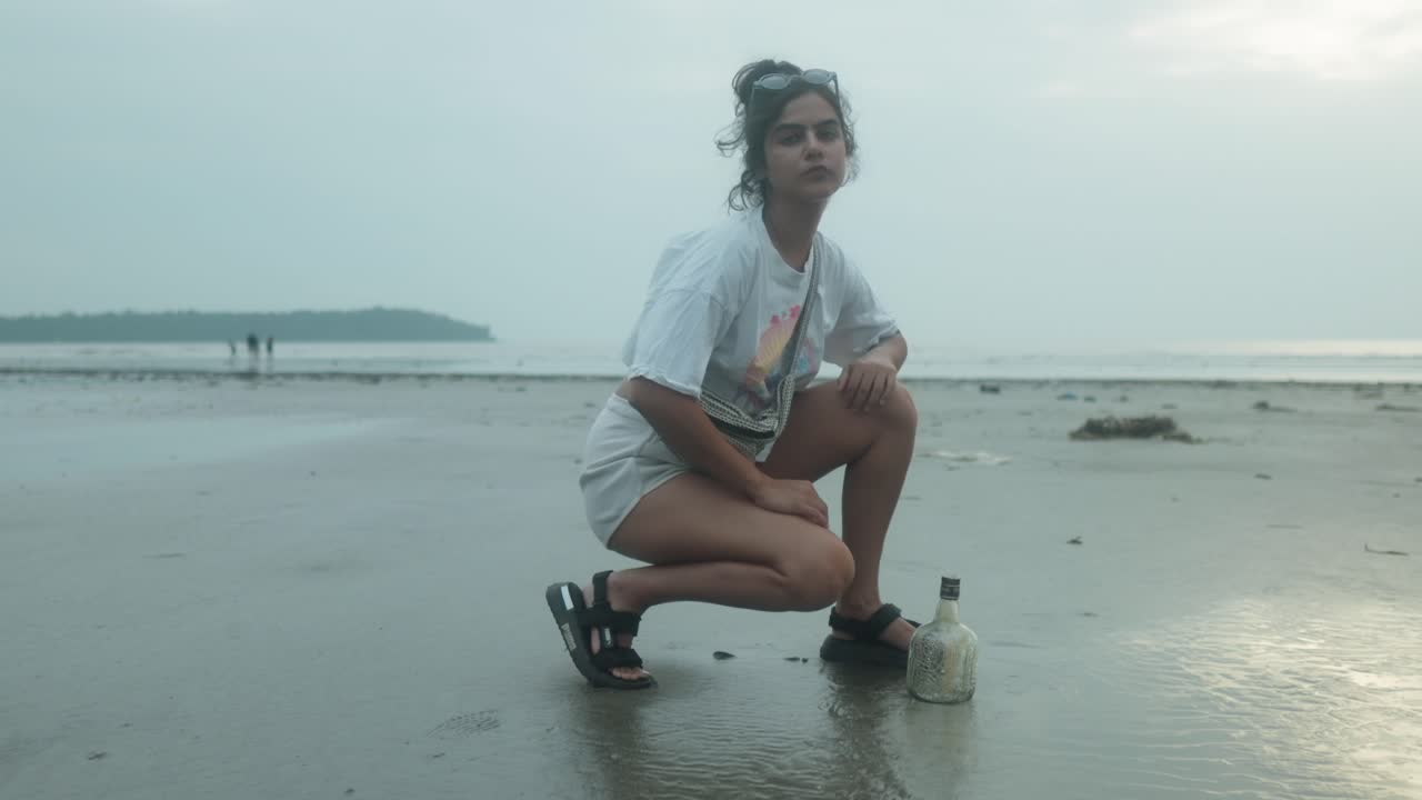 mujer joven explorando la playa junto a una botella hundida mientras ajusta su mochila