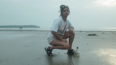 Mujer-Joven-Explorando-La-Playa-Junto-A-Una-Botella-Hundida-Mientras-Ajusta-Su-Mochila.