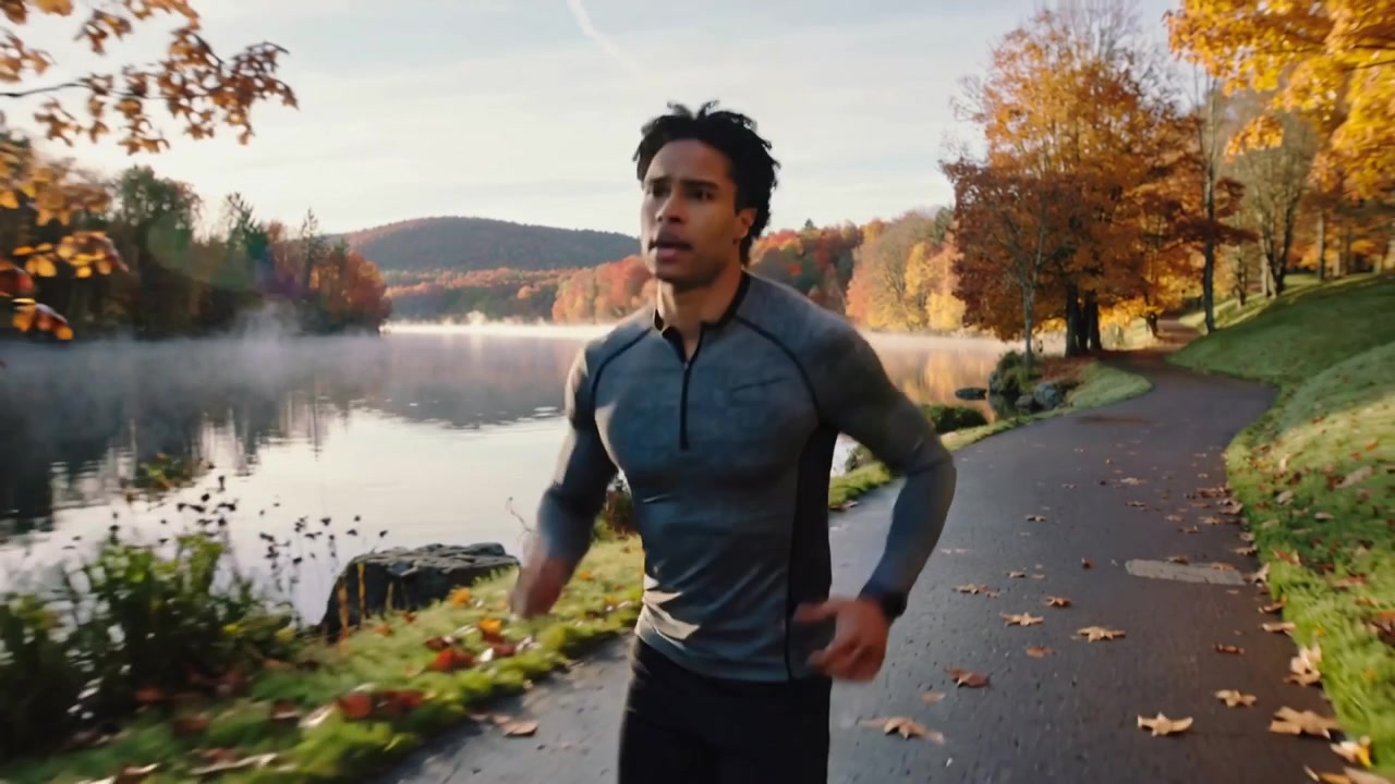 Un corridore maschio corre all'alba lungo un sentiero del lago, indossando una maglietta e un orologio per il fitness.