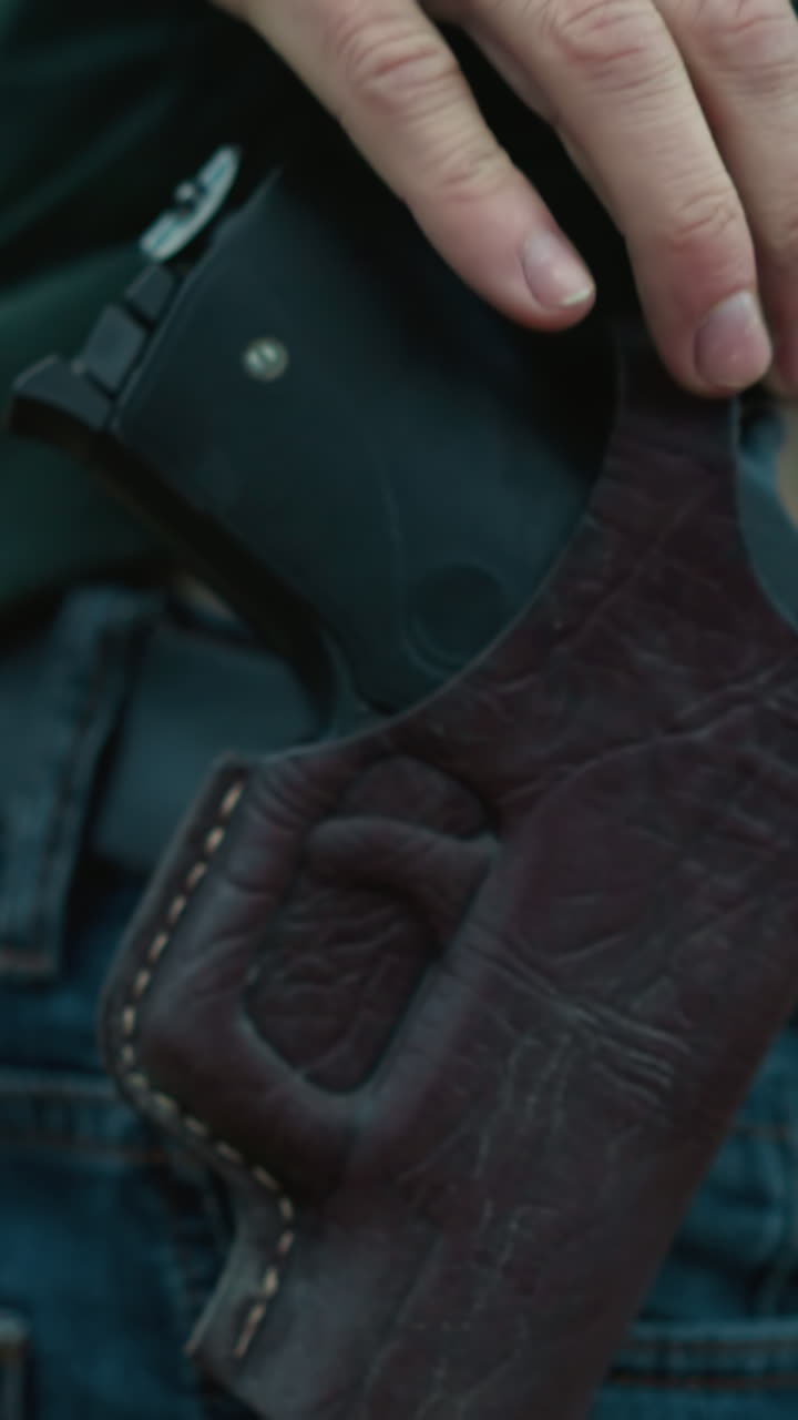 una vista de cerca de un hombre cargando una pistola, la escena se centra en las manos, la funda y parte de los vaqueros mientras se aleja, con un borrón que rodea