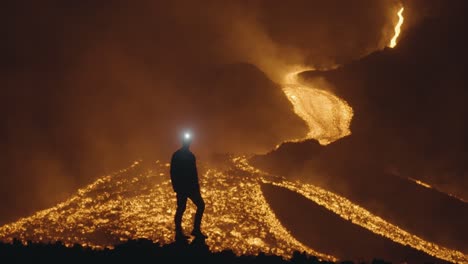 pacaya volcano, guatemala - a silhouette of a man with a headlamp gazing at the glowing rivers of lava in the night - handheld shot