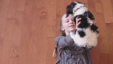 la niña acaricia a su adorable cachorro mientras yace en un suelo de madera.