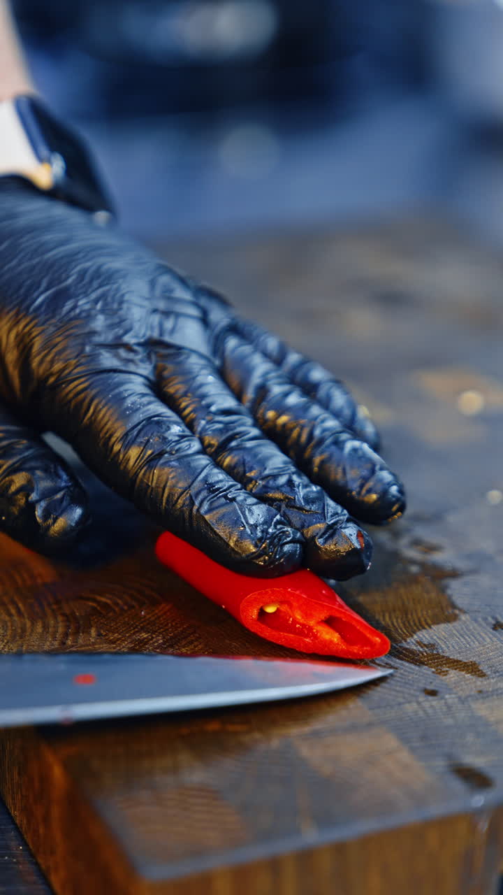 Chef cutting red hot chili pepper with a big knife. Cook preparing a dish. Close up. Vertical video.