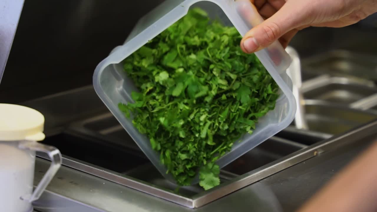 chef vertiendo cilantro picado en un recipiente listo para el servicio y el restaurante
