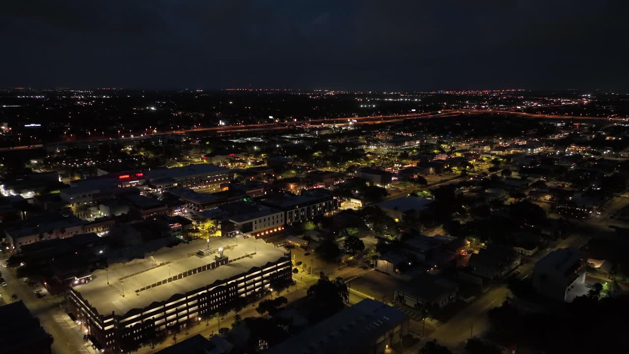 Tampa town, Florida. Bright city lights illuminate streets, buildings and parking structures. Urban landscape with traffic lines glowing in distance under dark sky. Aerial wide shot. United States