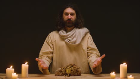 studio shot of man wearing robes representing figure of jesus christ preaching with bread and wine