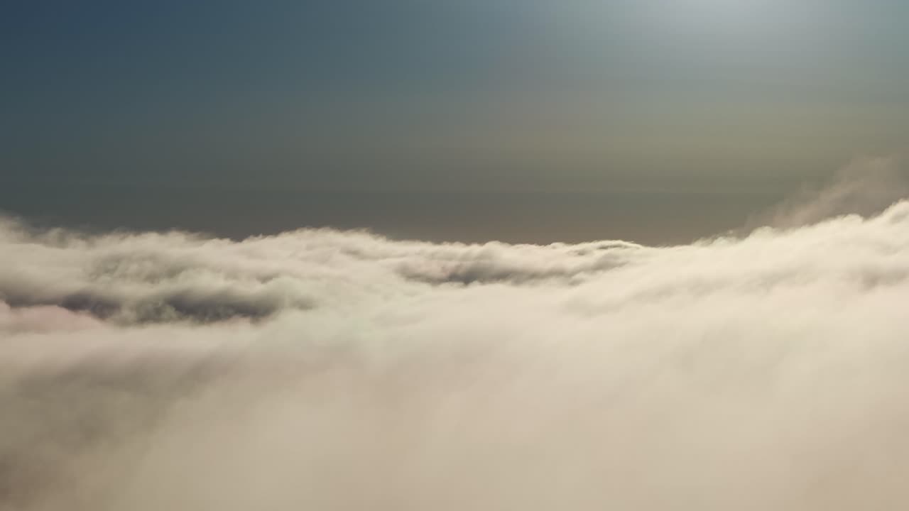 Solbelyste skytoppe strækker sig til horisonten under en blegblå morgenhimmel med blød dis.