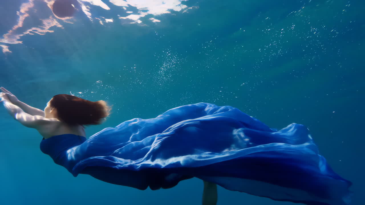 A woman in a blue dress gracefully swims underwater