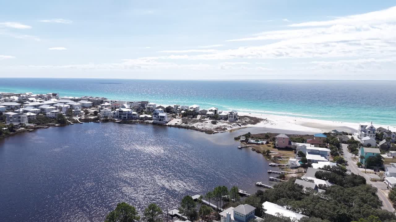 Volo frontale di drone sulla comunità di Eastern Lake, circondata da case e una stretta spiaggia barriera con un Golfo cristallino, Santa Rosa Beach, Florida, USA.