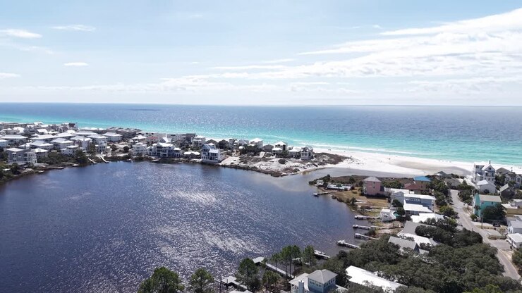 Volo frontale di drone sulla comunità di Eastern Lake, circondata da case e una stretta spiaggia barriera con un Golfo cristallino, Santa Rosa Beach, Florida, USA.