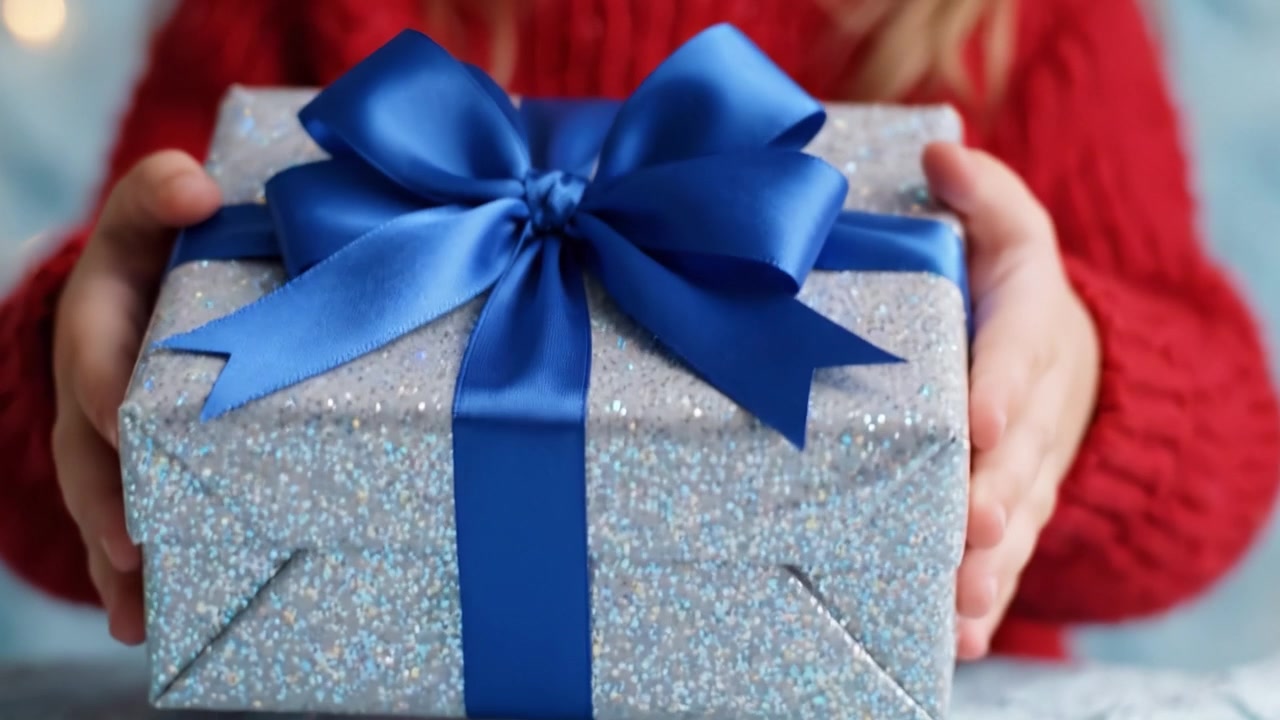 La gioiosa attesa di un bambino: Mani adorabili presentano un regalo scintillante con un fiocco blu, pieno di magia e sorpresa per un'occasione speciale.