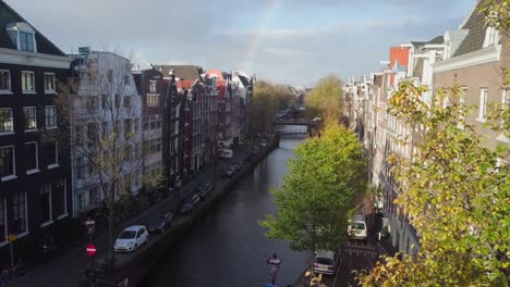 morning rainbow over amsterdam canals, tilting down, high angle reveal shot from behind trees