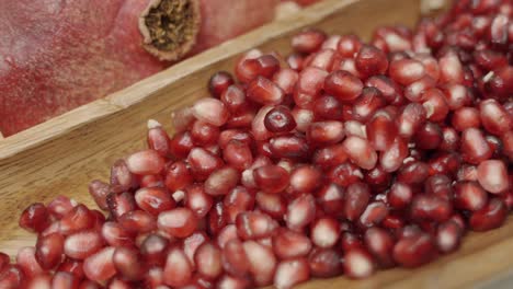 close up panning shot of pomegranate seeds inside wooden plate juicing and using fresh ingredients and fresh whole pomegranates