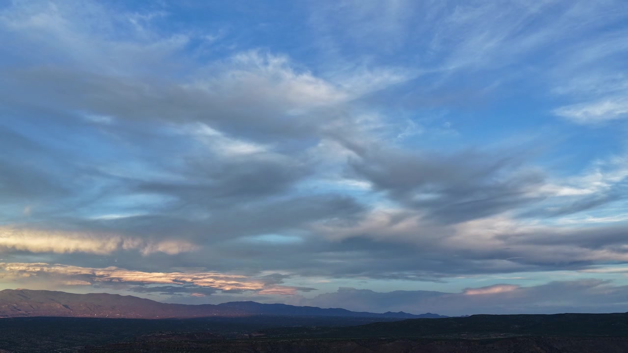 Timelapse 4K con drone di un sereno tramonto sud-occidentale vicino a Santa Fe. Raggi dorati serali si increspano tra le nuvole più basse e illuminano il bordo distante della catena montuosa Sangre de Cristo