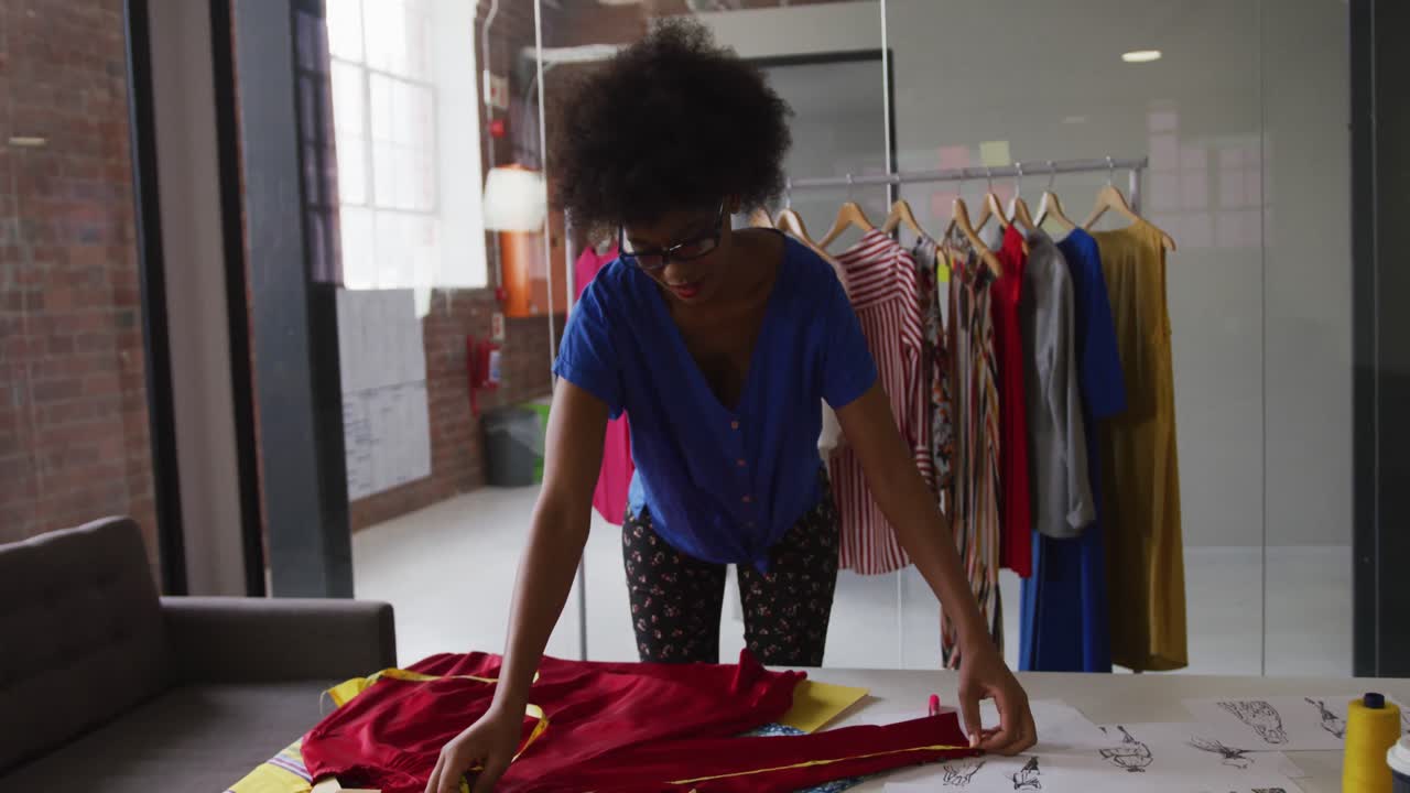 Stilista di moda afroamericana che prende le misure di un capo d'abbigliamento con un metro a nastro.