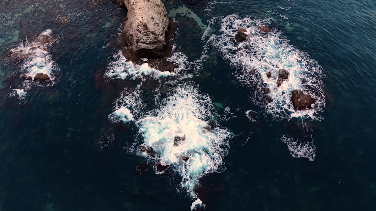 Large and small rocks scattered in deep blue water with white sea foam and ripples. Aerial view. of rocks in dark blue sea water with waves