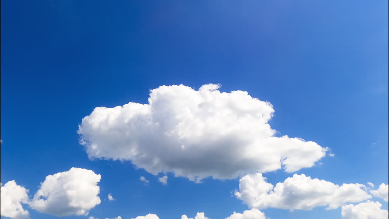 Fluffy soft clouds lit by the bright summer sky move by the horizon. Low angle view at the sky with cumulus clouds. Timelapse.