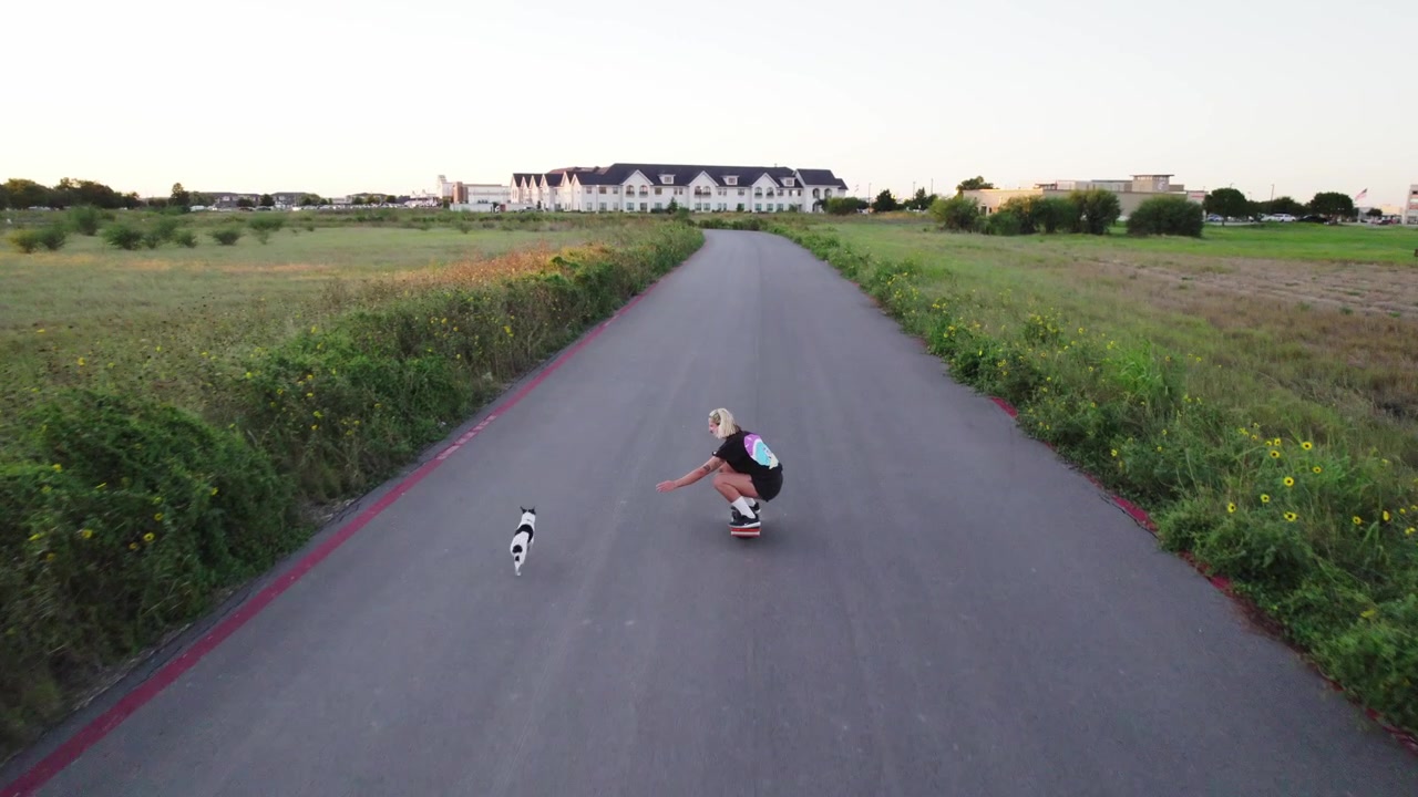 dog follows person on a onewheel down an empty road during sunset in the summer