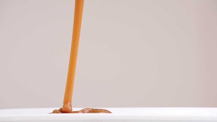 Glob of caramel drizzled onto white plate stacking ripples in slow motion back and forth on gray backdrop