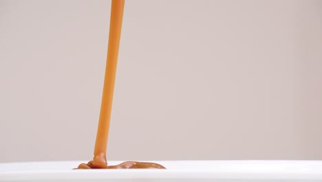 Glob-of-caramel-drizzled-onto-white-plate-stacking-ripples-in-slow-motion-back-and-forth-on-gray-backdrop