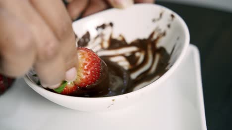 close up of dipping strawberries in melted chocolate to make chocolate covered strawberries valentines day beet muffin vegan recipe