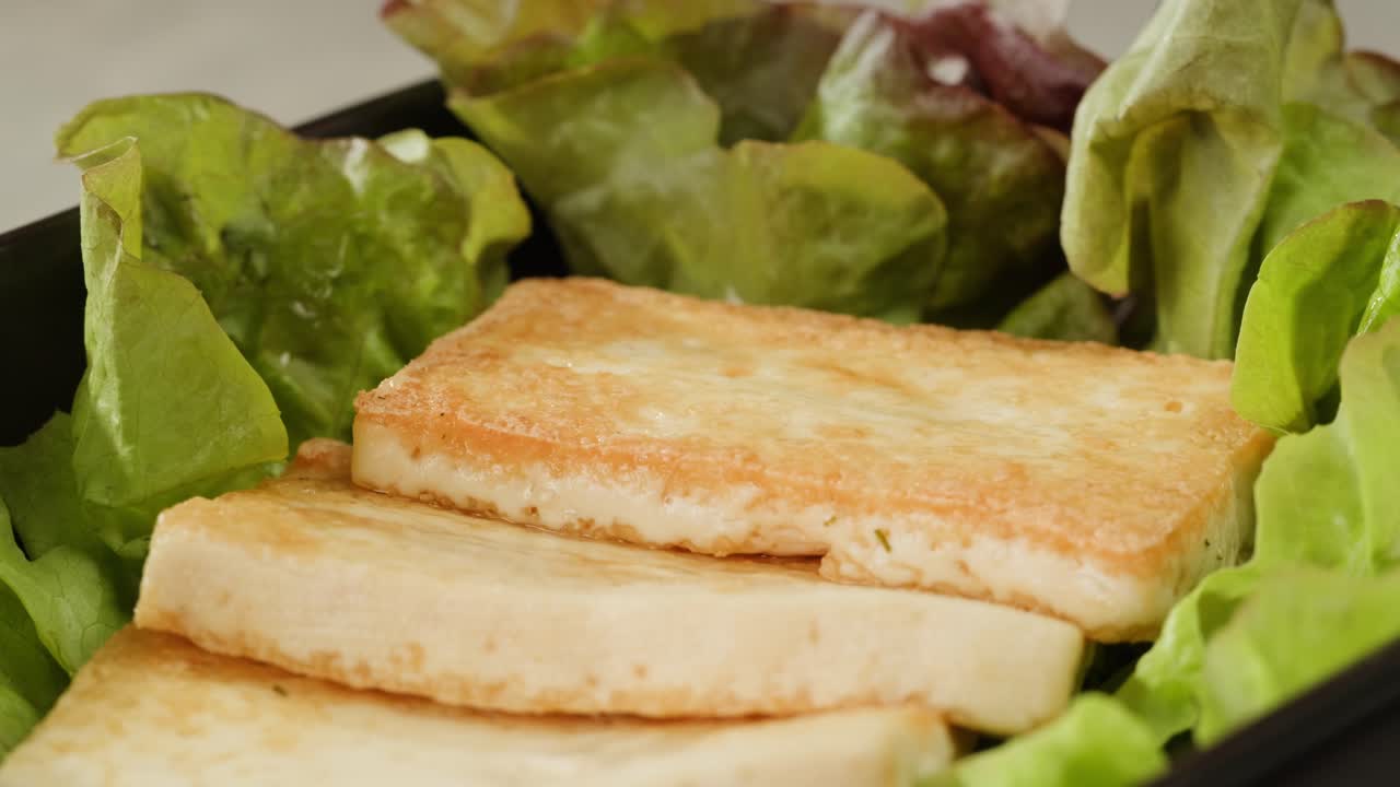 Fried tofu with sesame seeds and spices on cast iron pan, cooking japanese salad. Healthy ingredient for cooking vegan vegetarian diet food. Roasted tofu over black background.