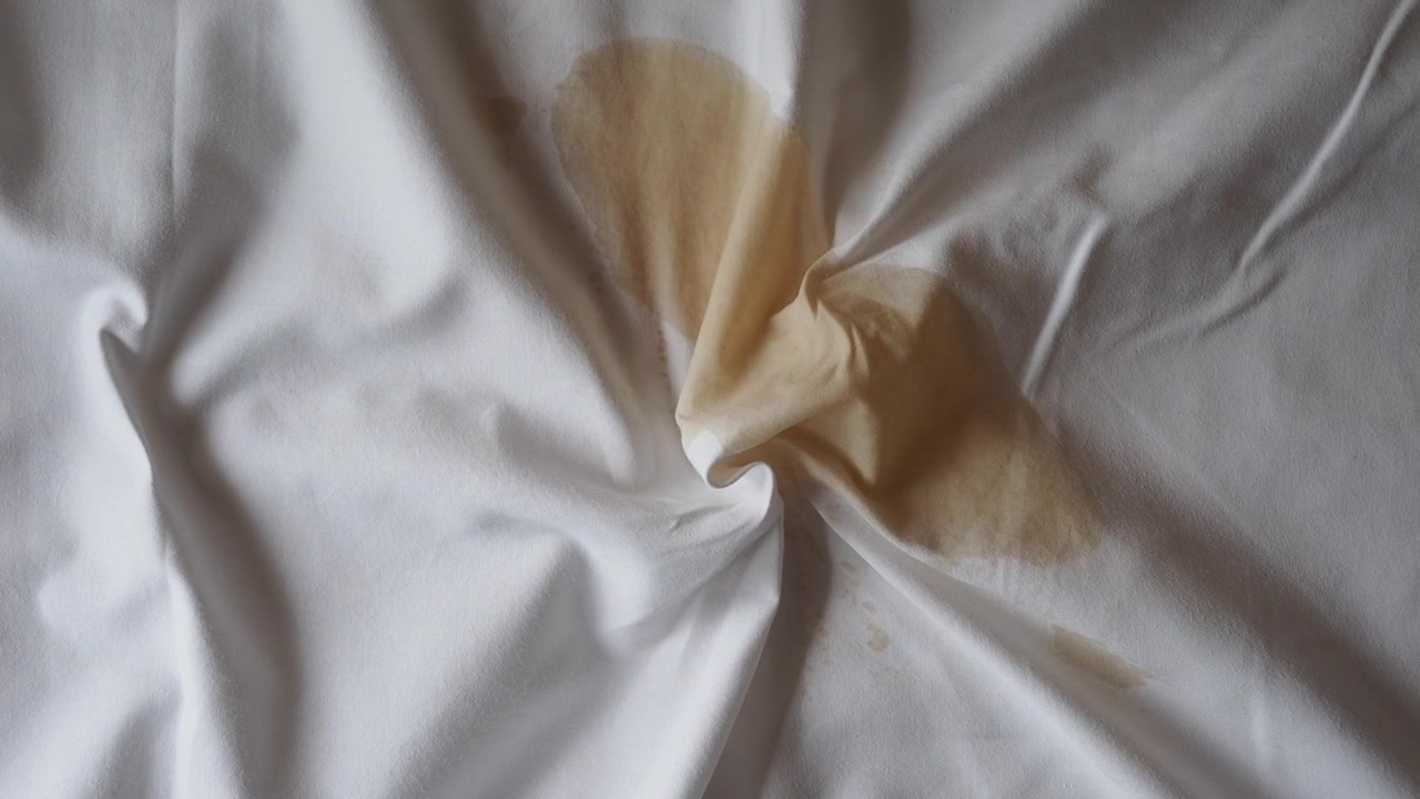 Mancha marrón húmeda sobre tela blanca arrugada