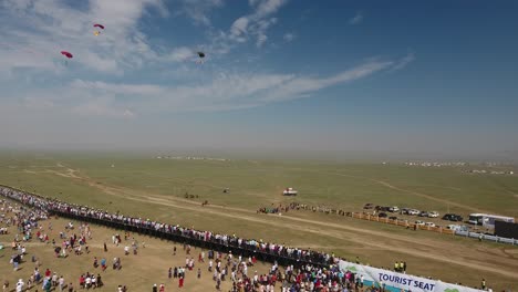 aerial drone shot of men landing in parachute after skydiving naadam festival